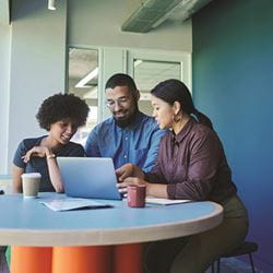 A group of three colleagues gathered around a laptop.